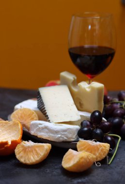 Üzümlü peynir tabağı, gri arka planda kırmızı şarap ve elma.