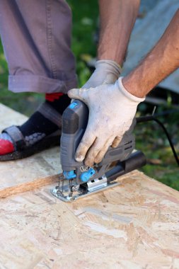 Marangoz tahta kesmek için yapboz kullanıyor. Bahçede tahta kesmek için yapboz kullanan bir işçi.