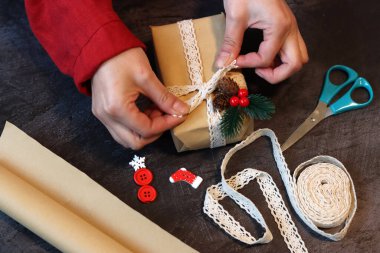 Kırmızı elbiseli bir kızın elleri dantel kurdeleyle hediye kutusunu süslüyor. Kadın eli hediye kutusunu tutuyor..