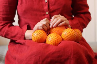 Woman in red dress with oranges in mesh bag on light background, closeup of hands clipart