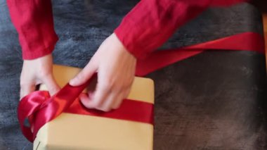 Kırmızı elbise giyen, hediye kutusunu kırmızı kurdeleyle süsleyen bir kadının elleri. Noel kutlaması kavramı. 