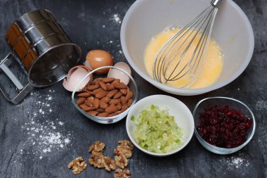 Kızılcık turtası yapmak için gerekli malzemeler - yumurta, un, şeker, fındık, gri arka planda kuru üzüm
