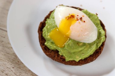 Kavrulmuş yumurta ve beyaz tabakta baharatlı avokado tostu.