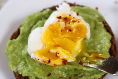 Kavrulmuş yumurta ve beyaz tabakta baharatlı avokado tostu.