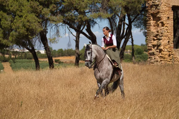 stock image Woman horsewoman, young and beautiful, performing cowgirl dressage exercises with her horse, in the countryside next to a ruined building. Concept horse riding, animals, dressage, horsewoman, cowgirl.