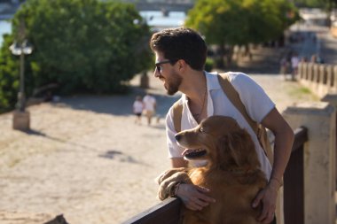 Young Hispanic man with beard, sunglasses and white shirt, leaning out with his dog leaning on a railing in funny attitude. Concept animals, dogs, love, pets, golden.