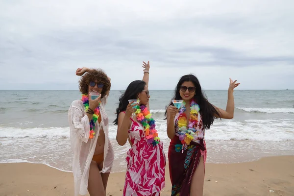 stock image Attractive mature woman with two young, pretty, brunette South American women in bikinis, sunglasses and flower necklaces dancing with glasses of blue wine. Concept vacation, friends, summer, drinks.