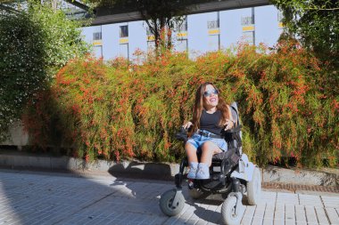 Hareket kabiliyeti düşük ve tekerlekli sandalyeli engelli bir kadın güneşli bir günde sokakta mutlu bir şekilde poz veriyor. Özürlülük, yetersizlik, yetersizlik, özel ihtiyaçlar.