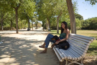Genç bir kadın, esmer, ince, yeşil tişört ve kot giymiş, köpeğinin yanındaki bankta oturuyor, mutlu ve sevgi dolu bir tavırla. Hayvanlar, hayvanlar, dostlar, aşk, köpekler, üreme.
