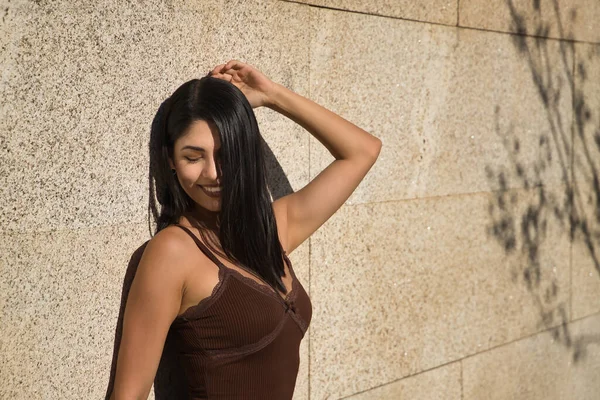 南美女人 年轻貌美 穿着一件棕色的连衣裙 以一种性感而挑衅性的姿态靠着墙摆姿势 概念美 — 图库照片