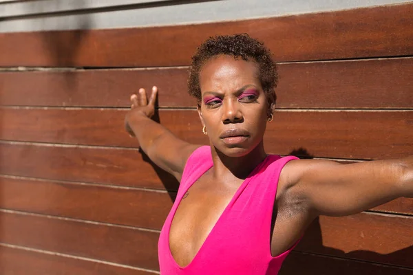 ピンクのTシャツを着たアフリカ系アメリカ人女性の肖像画 木製の板の背景にもたれて 真剣なジェスチャーと腕を開いています 概念の強化 — ストック写真