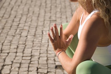 Orta yaşlı, yeşil taytlı, beyaz tişörtlü, meditasyon ve yoga egzersizleri yapan sarışın bir kadının elleri. Yoga, meditasyon, konsantrasyon, spor, farkındalık.