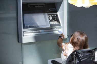 Hareket kabiliyeti düşük ve tekerlekli sandalyeli engelli bir kadın ATM 'den para çekmeye çalışıyor. Özürlülük, yetersizlik, özel ihtiyaçlar, mimari engeller.