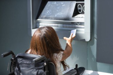 Hareket kabiliyeti düşük ve tekerlekli sandalyeli engelli bir kadın ATM 'den para çekmeye çalışıyor. Özürlülük, yetersizlik, özel ihtiyaçlar, mimari engeller.