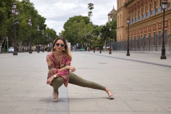 stock image Young, attractive and blonde woman, wearing cashmere shirt, green pants and sunglasses, posing crouched on the floor. Concept beauty, fashion, trend, model.