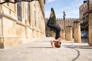 Orta yaşlı sarışın bir kadın, siyah bir mayo giyiyor, şehrin tarihi merkezinde meditasyon ve yoga egzersizleri yapıyor. Yoga, meditasyon, konsantrasyon, spor, farkındalık.