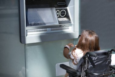 Hareket kabiliyeti düşük ve tekerlekli sandalyeli engelli bir kadın ATM 'den para çekmeye çalışıyor. Özürlülük, yetersizlik, özel ihtiyaçlar, mimari engeller.