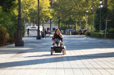 Hareket kabiliyeti düşük engelli bir kadın ve şehir merkezinde yürüyen tekerlekli sandalyeli küçük bir kadın. Özürlülük, yetersizlik, özel ihtiyaçlar, mimari engeller.
