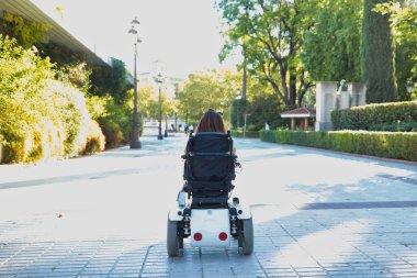 Engelli, hareket kabiliyeti düşük ve tekerlekli sandalyeli bir kadın şehir merkezinde arkadan görülüyor. Özürlülük, yetersizlik, yetersizlik, özel ihtiyaçlar.