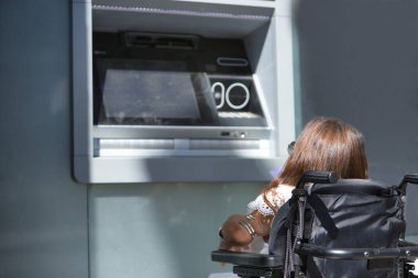 Hareket kabiliyeti düşük ve tekerlekli sandalyeli engelli bir kadın ATM 'den para çekmeye çalışıyor. Özürlülük, yetersizlik, özel ihtiyaçlar, mimari engeller.