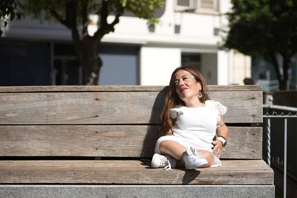 Woman with disability, reduced mobility and small stature sitting on a wooden bench, happy and relaxed sunbathing. Concept handicap, disability, incapacity, special needs, overcoming.