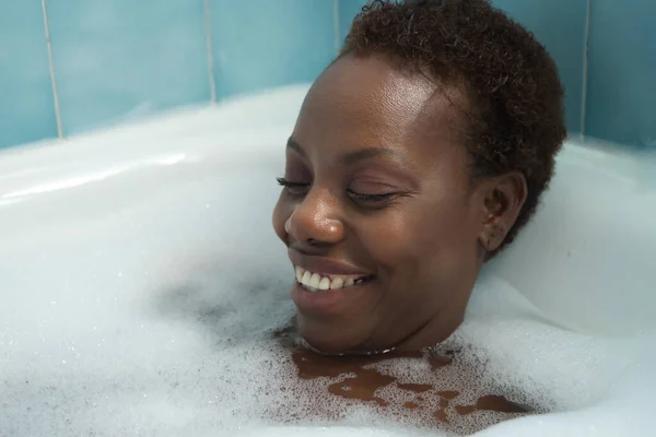 Portrait of African American woman, taking a bath with the bathtub full of foam, smiling happy and relaxed. Concept bath, relax, foam, soap.