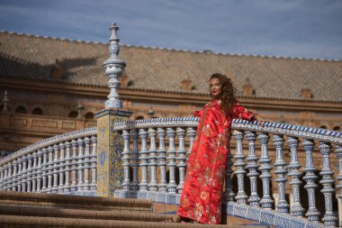 Altın ve gümüş ipliklerle işlenmiş tipik bir Fas kırmızı elbisesi içinde İspanyol meydanındaki fayanslı korkuluklara yaslanmış güzel bir genç kadın. Güzellik kavramı, etnik köken, tipik takım elbiseler, Arap.
