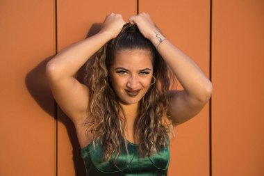 Latin ve İspanyol kız, genç ve güzel, yeşil gözlü ve büyük kirpikli, komik bir tavırla saçını çekiyor. Güzellik, moda, jestler, saç stilleri, kıvırcık.