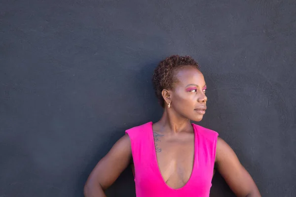 Portrait of African American woman in a pink T-shirt and pink eyeshadow, looking to her left on a gray background. Concept empowerment, independence, struggle, power.