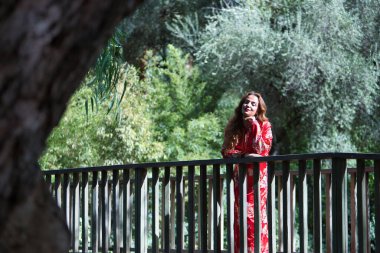 Tipik Fas kırmızısı takım elbiseli güzel bir kadın, altın ve gümüş ipliklerle işlenmiş, açık hava parkında korkuluklara yaslanmış. Güzellik kavramı, etnik köken, tipik takım elbiseler, Marakeş, Arap.