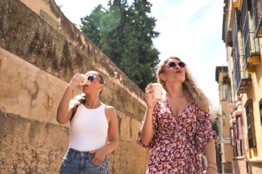 İki kadın, genç ve güzel, ellerinde güneş gözlüğü ve kahve bardaklarıyla gülümseyen ve mutlu bir şekilde, bir şehir caddesinde yürüyüp sohbet ediyorlar. Dostluk, dostluk, suç ortaklığı, mutluluk kavramı.