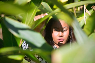 Portrait of a young, beautiful, Latin and South American woman, within a leafy group of green leaves, receiving the sun's rays between the hollows of the leaves and making different expressions.