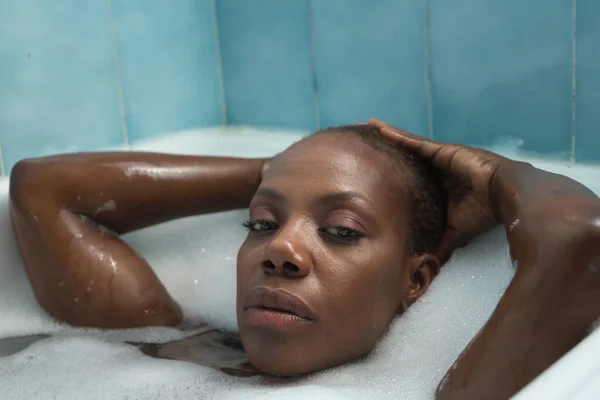 非洲裔美国妇女的画像 双手放在头上 用满是泡沫的浴缸洗澡 非常轻松 概念洗浴 — 图库照片