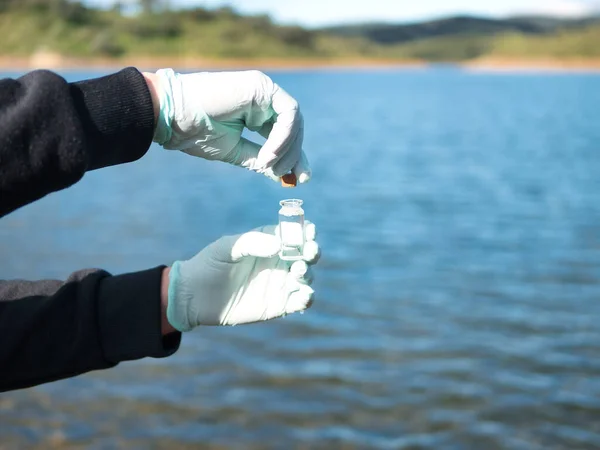 Laboratuvarda analiz için kirlenmiş su numunesiyle kavanozu kapatan eller. Konsept kirliliği, analiz, çevre.