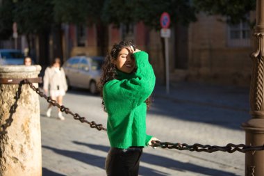 Genç, güzel, kıvırcık saçlı, yeşil boğazlı kazaklı, şehvetli ve çapkın tavırlarıyla saçlarına dokunan esmer bir kadın. Güzellik, moda, sonbahar, kış, soğuk, şehvet kavramı.