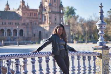 Young, beautiful, Latin and South American woman with leather jacket and top and black jeans leaning on a tiled railing with seductive and flirtatious look. Concept beauty, fashion, diversity, latina