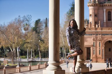 Young, beautiful, Latin and South American woman in short dress with zebra pattern, climbing a brick wall between two marble columns, posing sensual and attractive as a super model.
