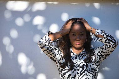 Portrait of a young, beautiful, Latin and South American woman with a dress with zebra-like pattern, receiving the sun's rays between the hollows of the leaves and making different expressions.