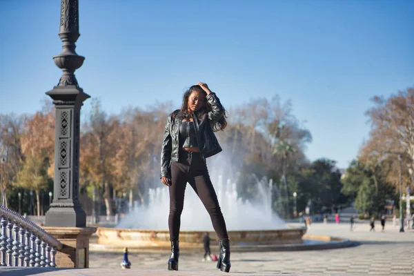 Young, beautiful, Latin and South American woman with leather jacket and top, jeans and platform shoes, touching her hair posing sensual and beautiful. Concept beauty, fashion, diversity, latina.