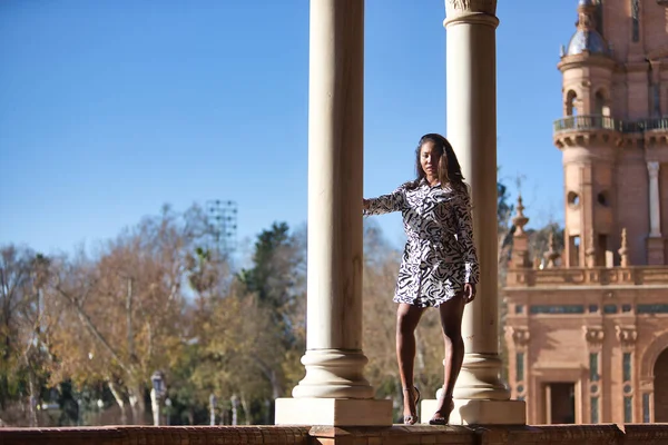 stock image Young, beautiful, Latin and South American woman in short dress with zebra pattern, climbing a brick wall between two marble columns, posing sensual and attractive as a super model.