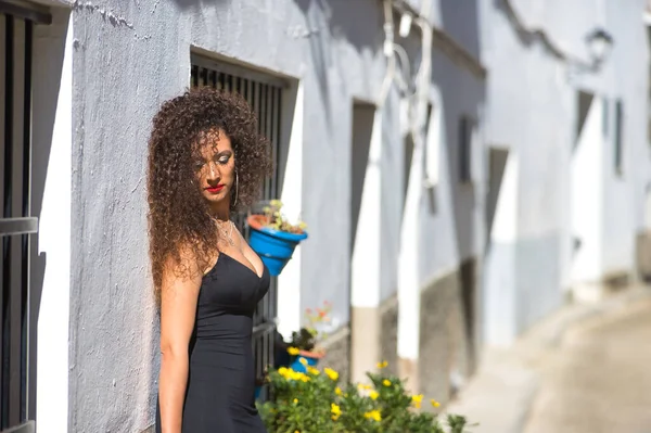 若い女性 美しい ブルネット 巻き毛で 黒のドレスとヒールで 単独で悲しい 典型的な地中海の村で白い家にもたれて 概念的なファッション 美しさ 悲しみ — ストック写真