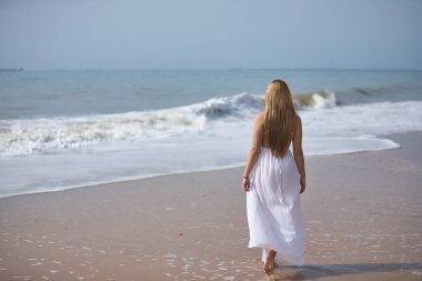 Genç, güzel, beyaz elbiseli sarışın bir kadın, yalnız bir sahilde yürüyor, rahat ve sakin, arkadan görülüyor. Huzuru, huzuru, yalnızlığı, kendini bulmayı kabul et..