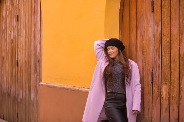 stock image Young woman, beautiful, straight brown hair, sweater, coat and black beret, leaning on a wooden door, happy and carefree. Concept beauty, fashion, autumn, winter, cold.