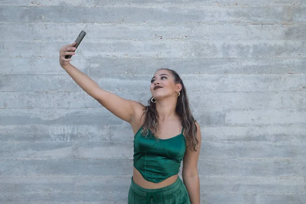ラティーナとヒスパニック系の女の子 若くて美しい 彼女の携帯電話でビデオを記録 灰色の背景に面白いジェスチャーを作ります コンセプトモバイル スマートフォン ビデオ アプリ レコード — ストック写真