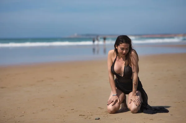 魅力的な若い女性は 青い目 黒の水着とサロンを着て 静かで悲しい ビーチの海岸にひざまずいて 概念静けさ 悲しみ うつ病 — ストック写真