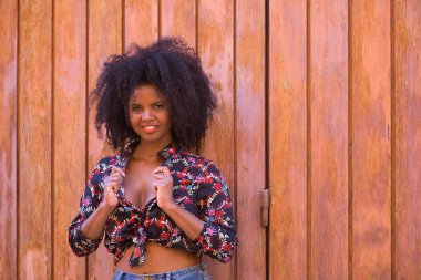 Genç bir kadın, güzel ve siyah saçlı, çiçekli gömlekli tahta bir tahta kapıya yaslanmış, şehvetli, kışkırtıcı ve çapkın bir tavırla. Güzelliği kavrayın, şehveti, kışkırtın, flört edin..