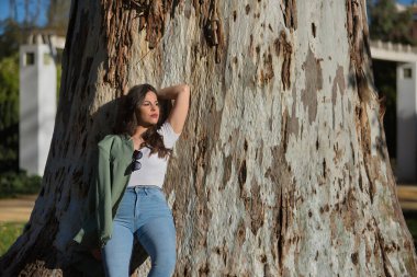Genç ve güzel bir kadın, İspanyol, kahverengi saçlı, yeşil ceketli ve kotlu, sonsuzluğa bakıyor, rahat ve sakin, kocaman bir ağacın gövdesine yaslanmış. Yalnızlık kavramı, rahatla, sakinleş..