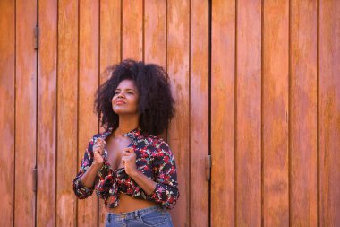 Genç bir kadın, güzel ve siyah saçlı, çiçekli gömlekli tahta bir tahta kapıya yaslanmış, şehvetli, kışkırtıcı ve çapkın bir tavırla. Güzelliği kavrayın, şehveti, kışkırtın, flört edin..