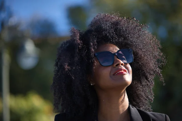 Stock image Portrait of young, beautiful, black woman with afro hair, with jacket and sunglasses, looking at the sky, grateful, praying. Concept gratitude, praying, current, modern.