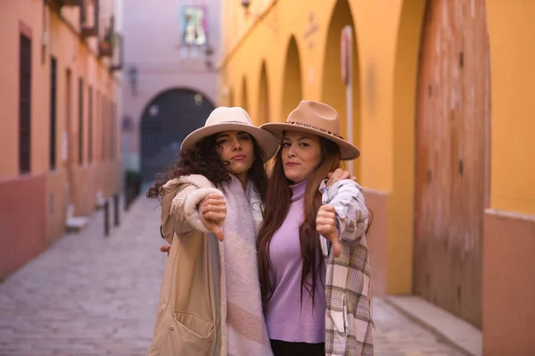 Dwie Kobiety Młode Piękne Kapeluszach Płaszczach Objął Kciuki Dół Znak — Zdjęcie stockowe